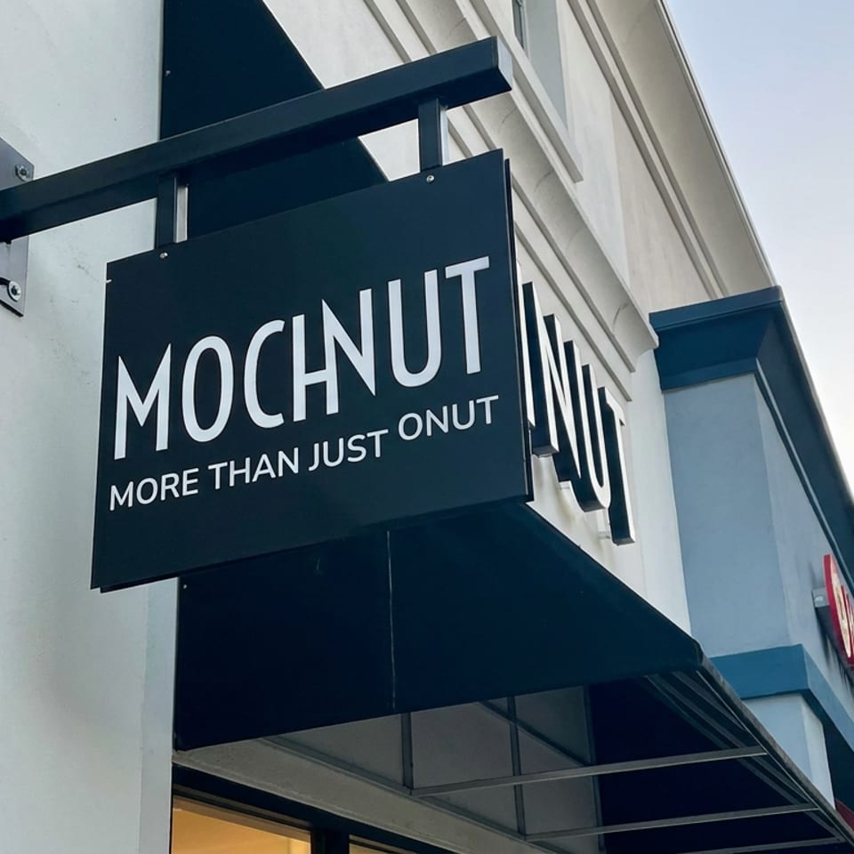Exterior sign for MOCNUT donut shop reading “More Than Just Onut,” mounted above the storefront entrance.