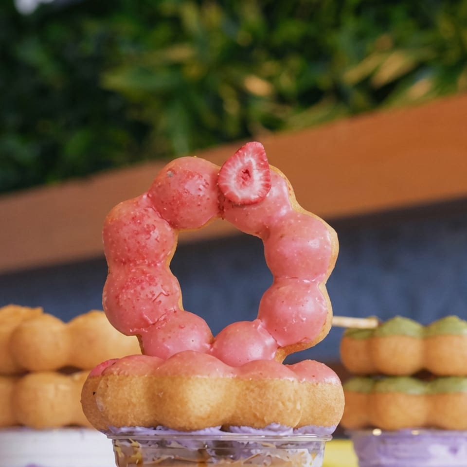 Pink ring-shaped frozen dessert topped with a strawberry slice, served on a golden pastry in a clear cup.