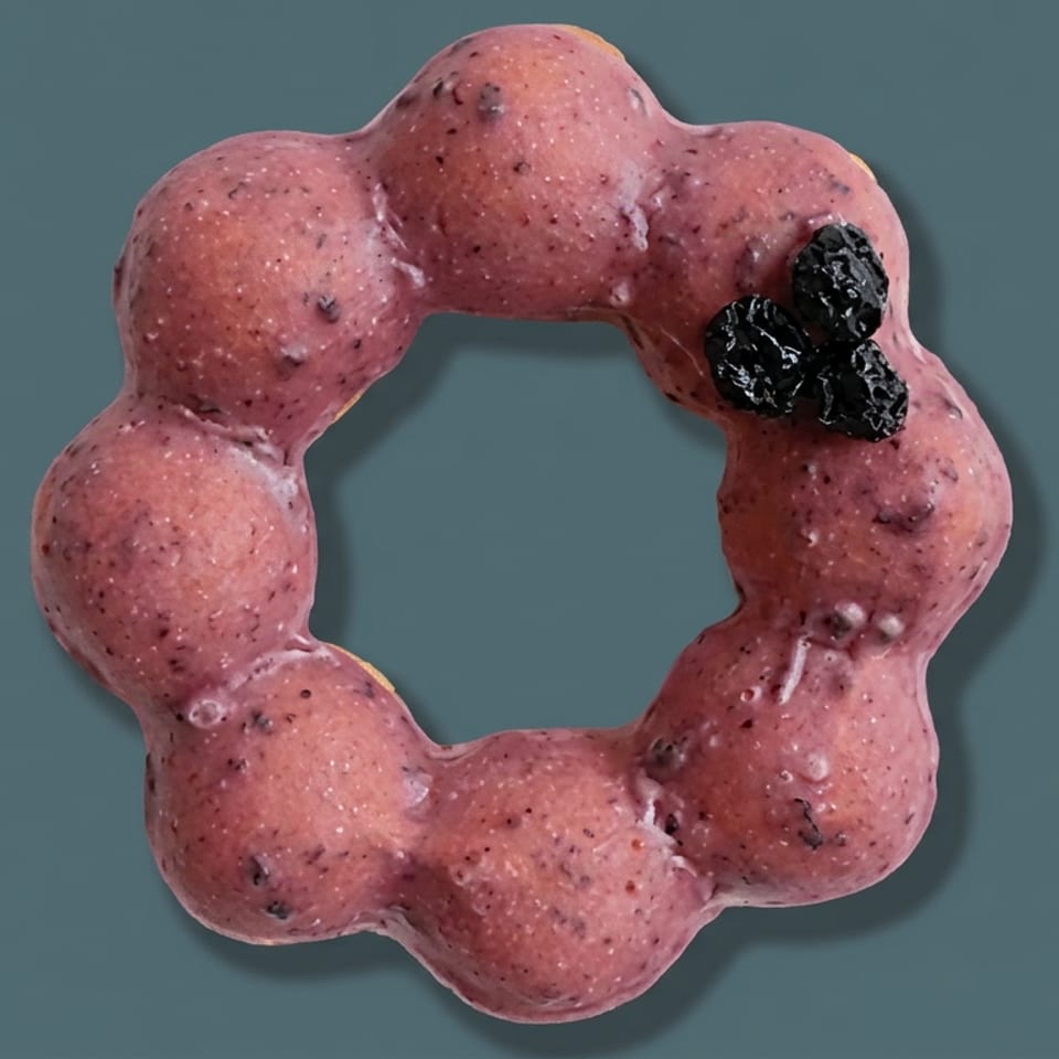 Pink berry-coated ring-shaped dessert topped with blackberries on a dark teal background.